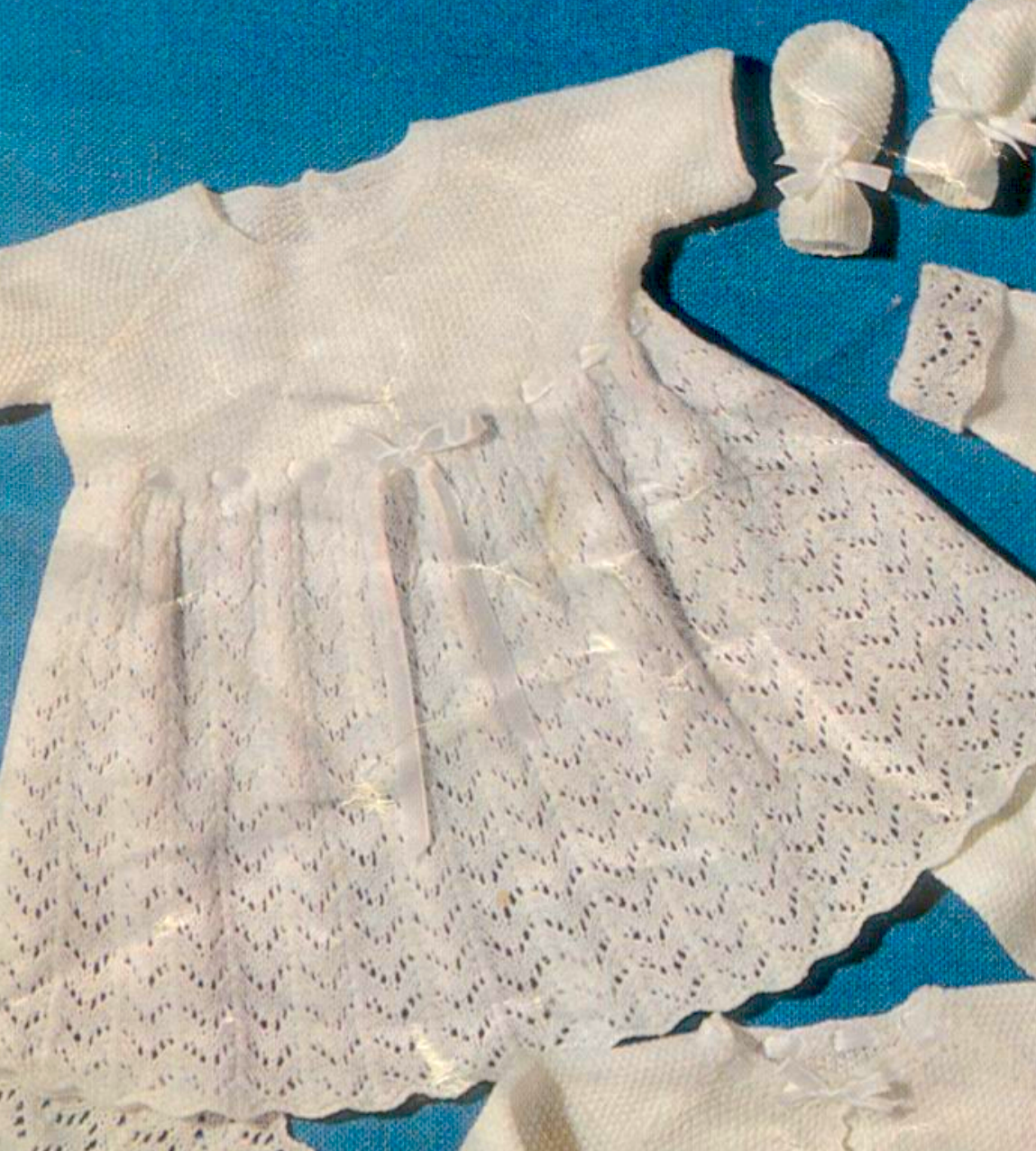 Close-up of baby dress in moss stitch with lace panels. Restored vintage 1960s baby layette knitting pattern in 3-ply.