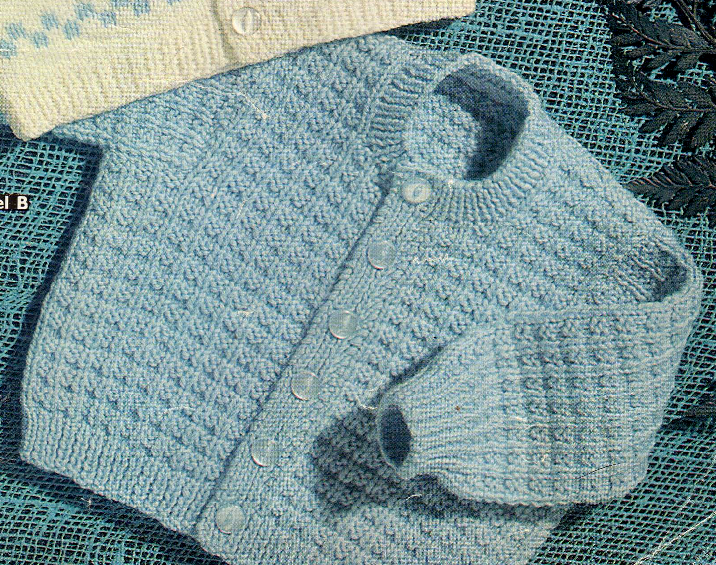 Close-up of baby boy round neck cardigan in all-over textured stitch pattern. Restored vintage 1970s knitting pattern in DK.