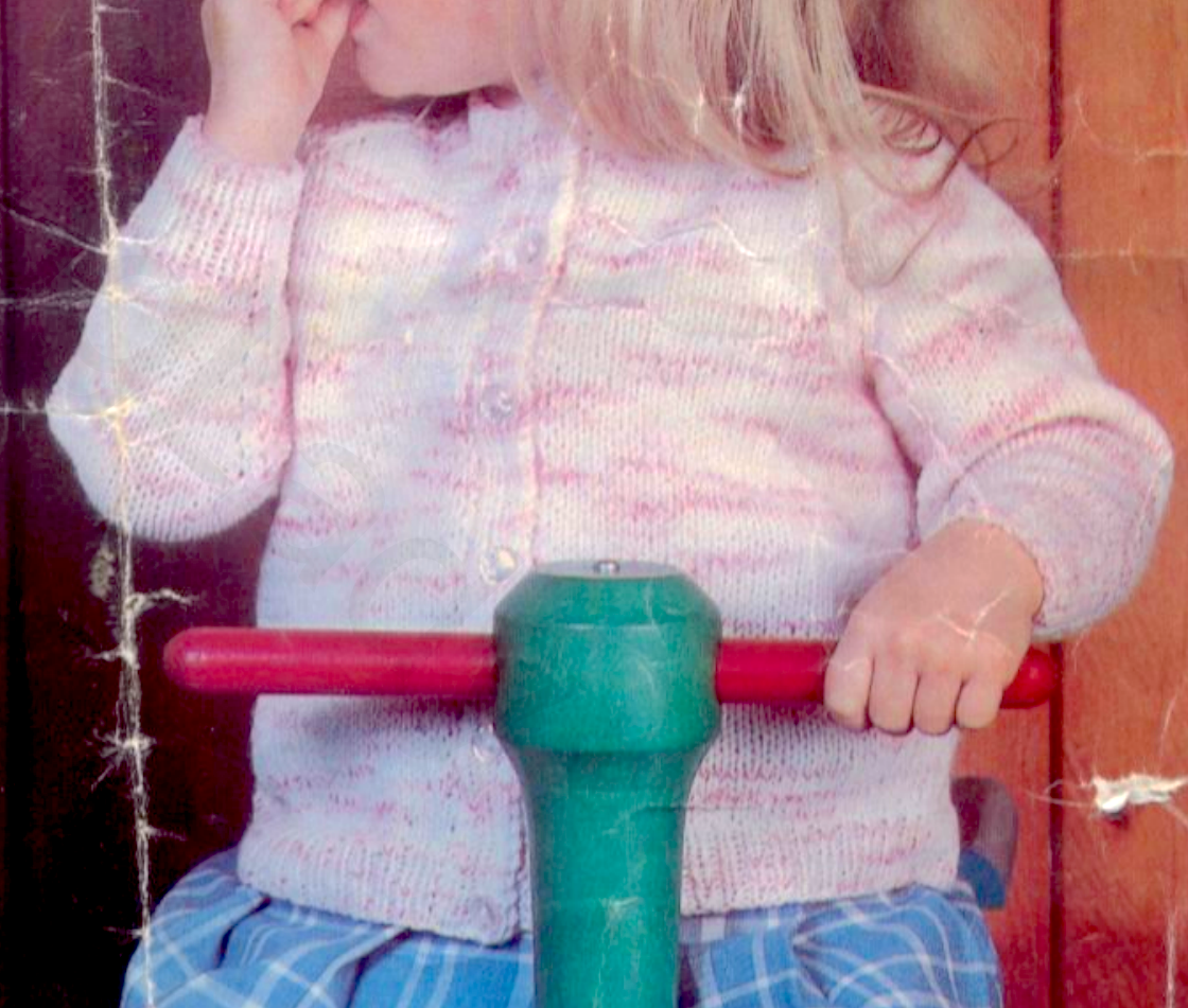 Close-up of vintage 1970s baby raglan cardigan with round crew neck. Restored knitting pattern in DK — worked flat in panels and seamed.
