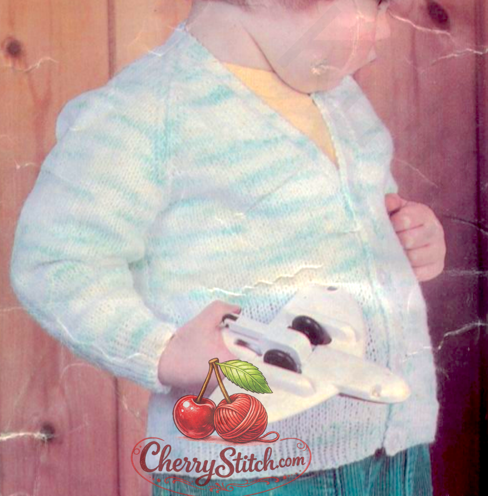 Close-up of vintage 1970s baby raglan cardigan with classic V-neck. Restored knitting pattern in DK — worked flat in panels and seamed.