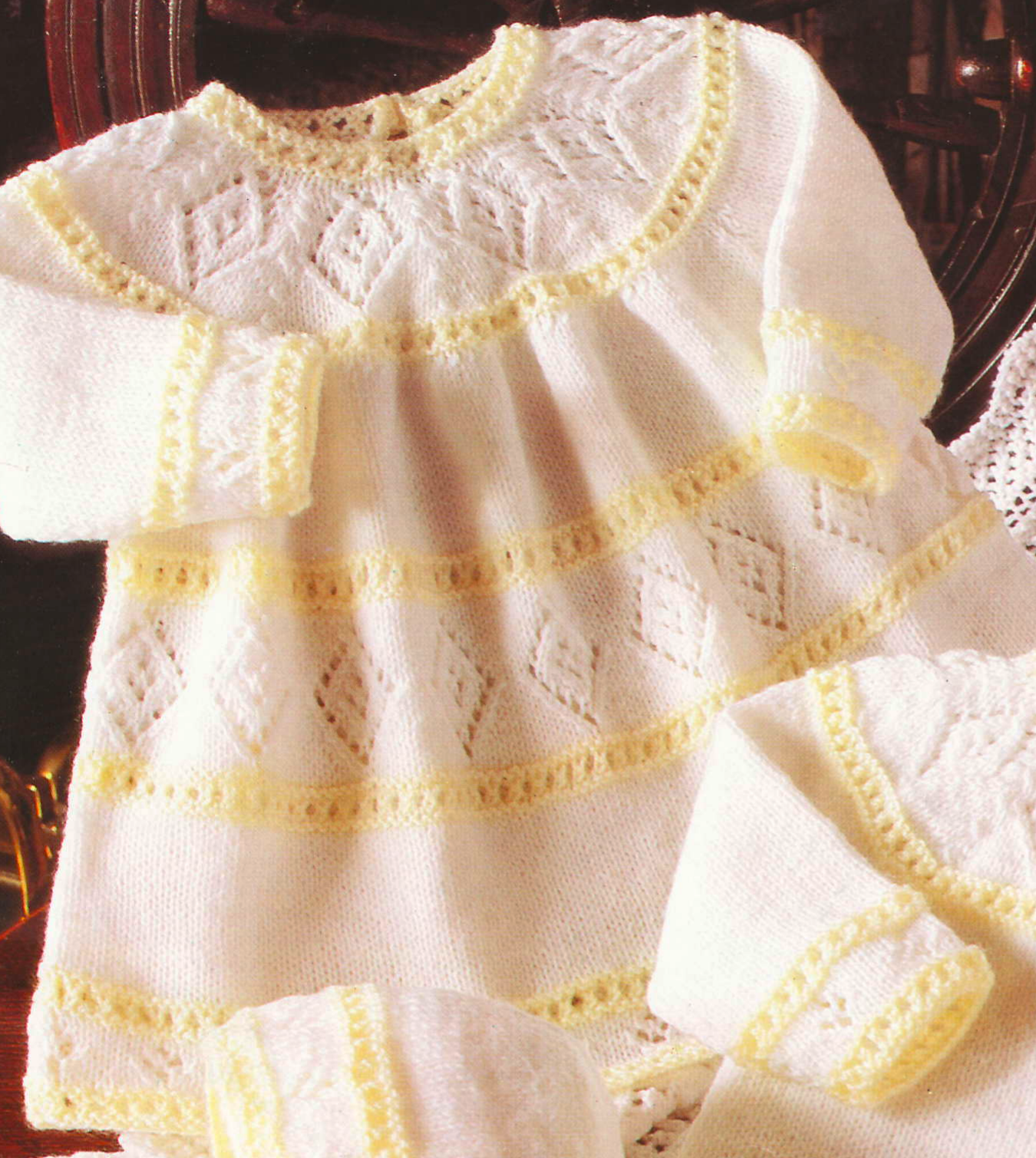 Close-up of knitted baby girl lacy diamond dress – restored vintage 1980s layette pattern in white and yellow 4-ply